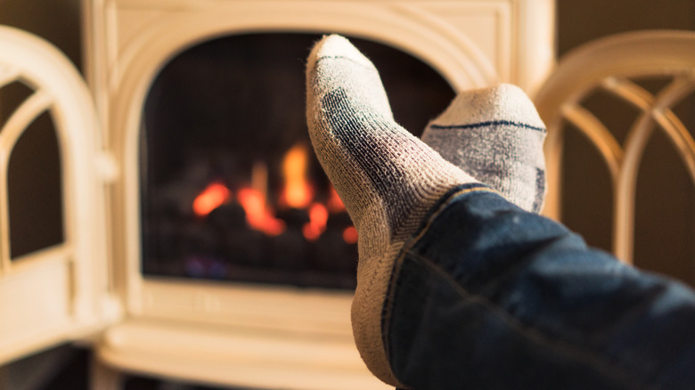 A person wearing socks warms their feet near a gas fireplace