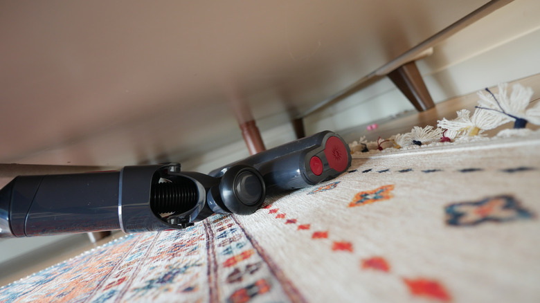 Vacuum being used to clean under large piece of furniture
