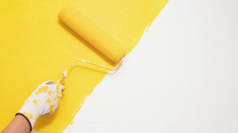 Person painting white wall yellow