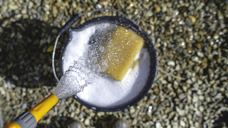 a hose pouring water into a soapy bucket in preparation for washing gravel stones