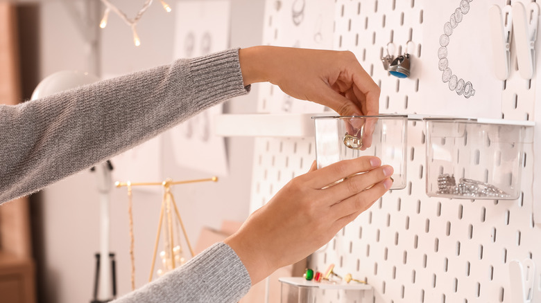 A woman's hands placing jewelry on a peg board attachment