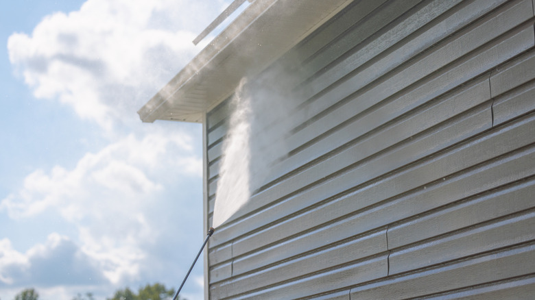 Worker pressure washing house