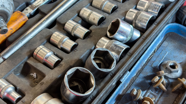 A close-up of a socket toolkit covered in dirt and dust with sockets haphazardly strewn about.