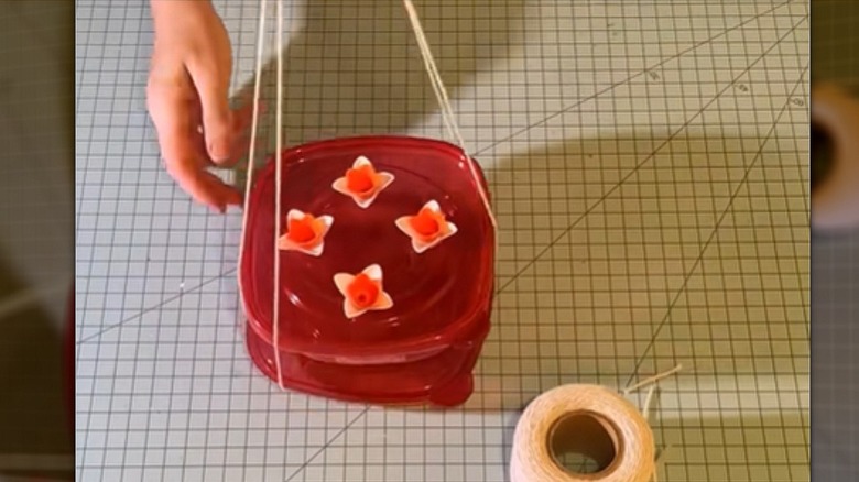 A DIY hummingbird feeder hangs in a harness made of string.