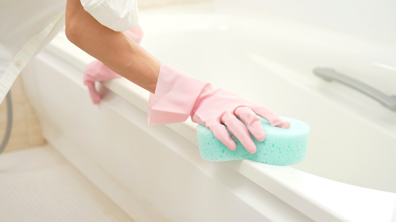 Woman's hands cleaning bathtub with a sponge