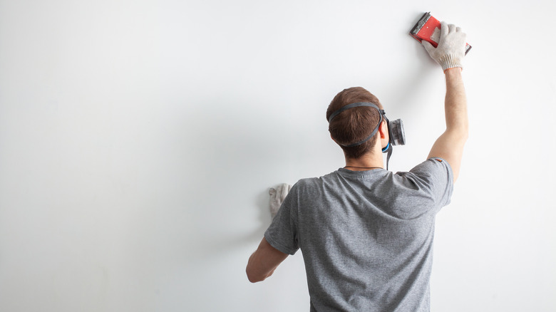 masked worker sanding wall