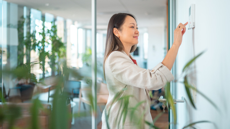 Woman adjusting thermostat with houseplants in background