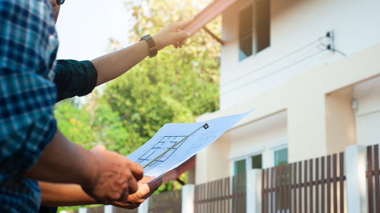 A man holding blueprints for a home standing outside with a person pointing at a roof