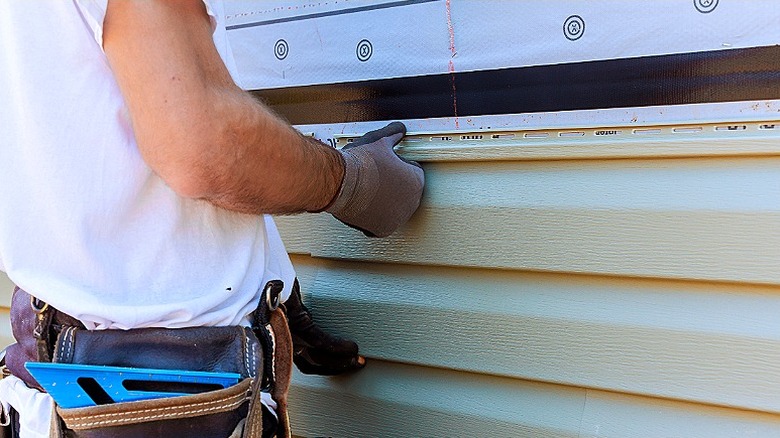 A contractor works on a home with beige vinyl siding
