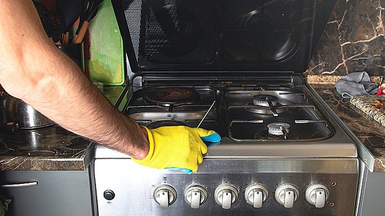 Close-up of a person holding a screwdriver in their right gloved hand and looking at the burners of a gas stove