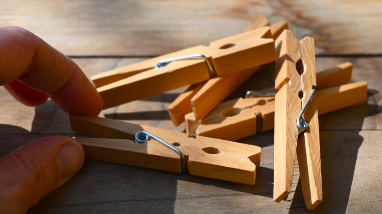 A hand holding a wooden clothespin on a table with other wooden clothespins in a pile.