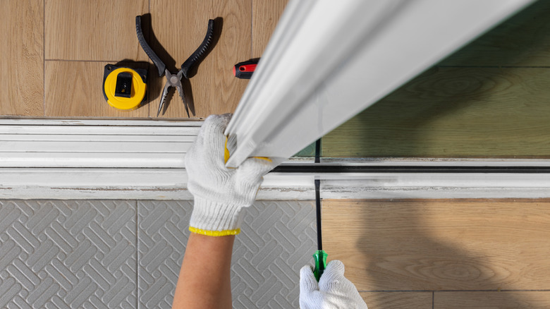 A worker wearing a pair of gloves adjusts a sliding glass door inside a white track