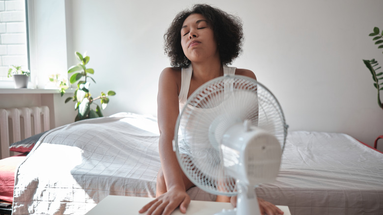 Woman trying to cool off by the fan while sitting on a bed