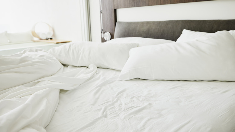 An unmade bed with white sheets and pillows
