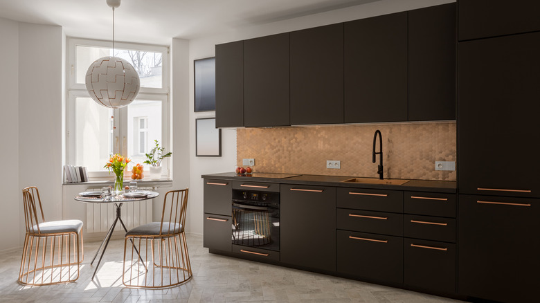 A modern kitchen with black cabinetry and a copper tiled backsplash