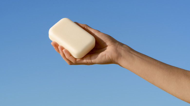 Female hand holding bar of soap against blue sky.