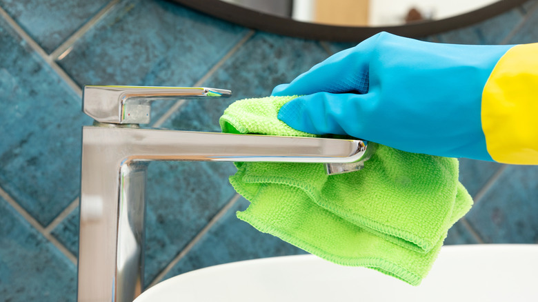 Person with glove cleaning a sink faucet