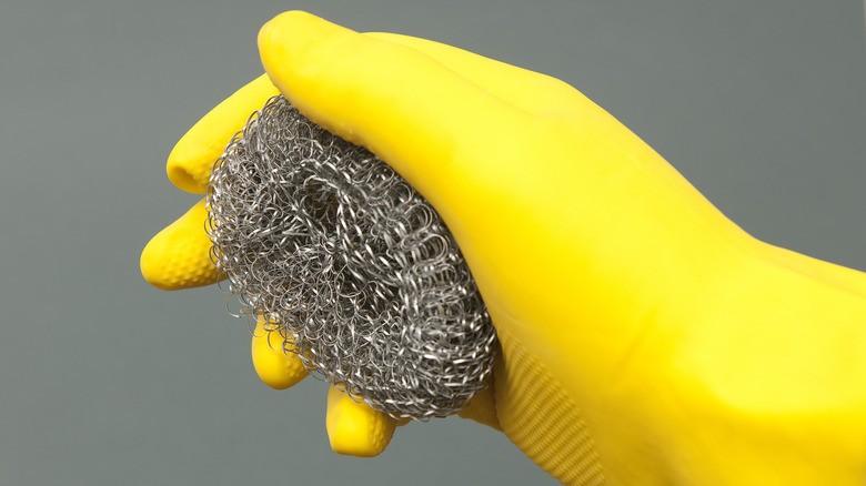 Yellow gloved hand holding steel wool