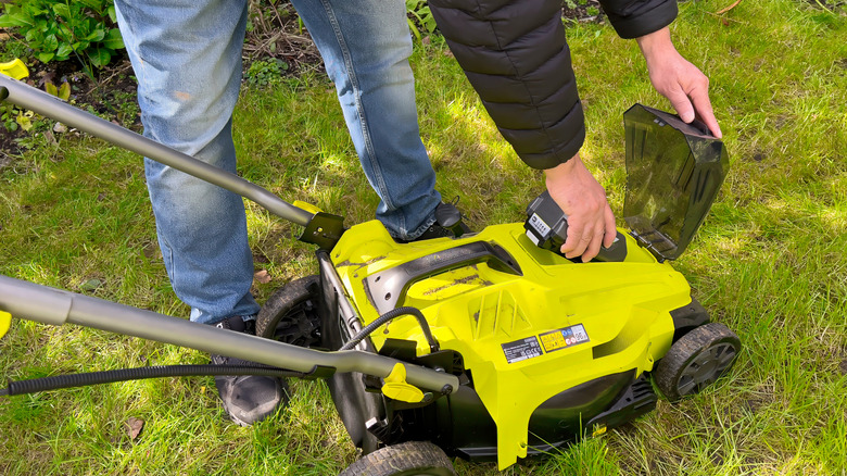 person inserting battery into lawn mower