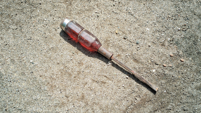 A weathered screwdriver with a clear red plastic handle