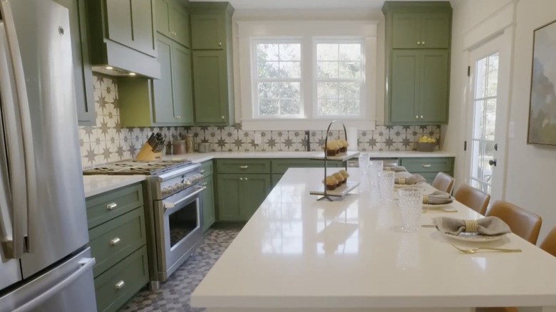 A bright kitchen with white stone island, sage green cabinetry, and geometric green and white backsplash tile