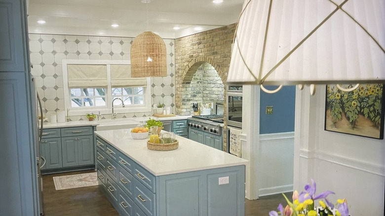 A light, modern kitchen with dusty blue cabinetry and tile walls next to a brick over-stove arch.