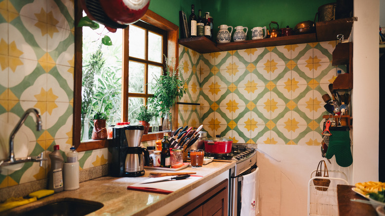 An eclectic kitchen with appliances on the counters and a colorful green and yellow tile backsplash.