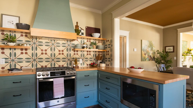 A cozy, rustic kitchen with a cherry tile backsplash, teal cabinets, and butcher block counters.