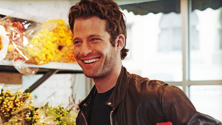 Nate Berkus smiles while in a floral shop with flowers in the background.