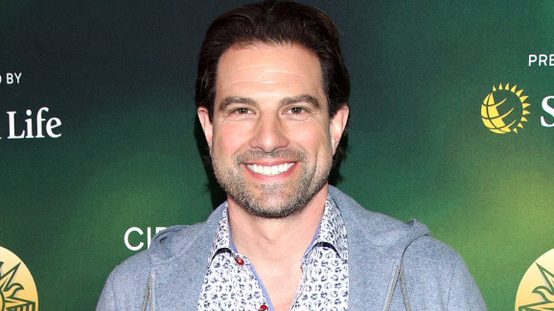 TV host Scott McGillivray at an event with a green logo-filled billboard behind him.