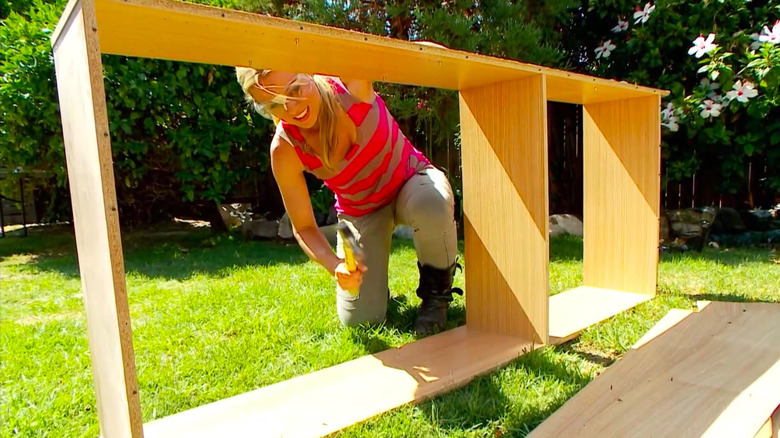 A woman kneeling outside woodworking.