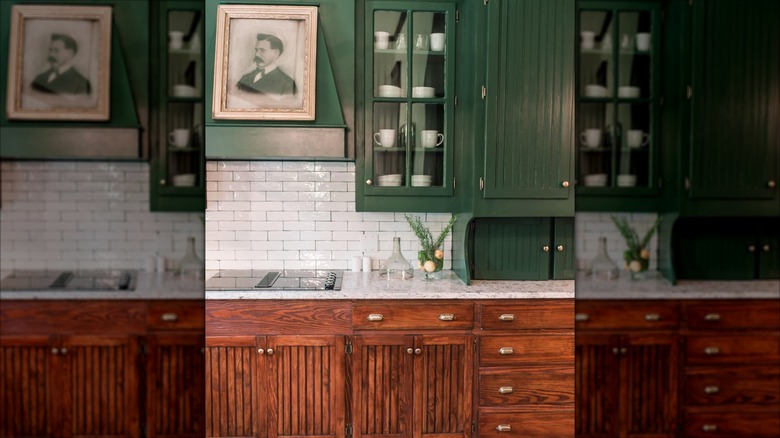 Beadboard kitchen cabinets with green upper cabinets and wood lowers with antique art on the range hood