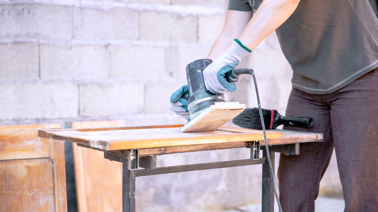 A man using a sander to remove finish from a cabinet door