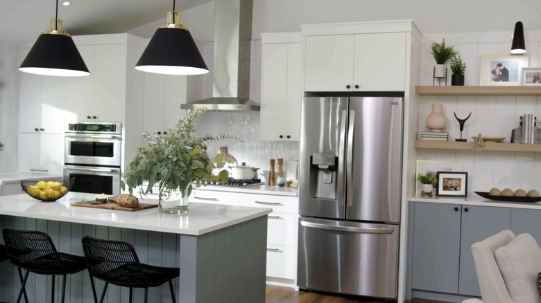 A kitchen with white cabinets and an island with black pendant lights overhead
