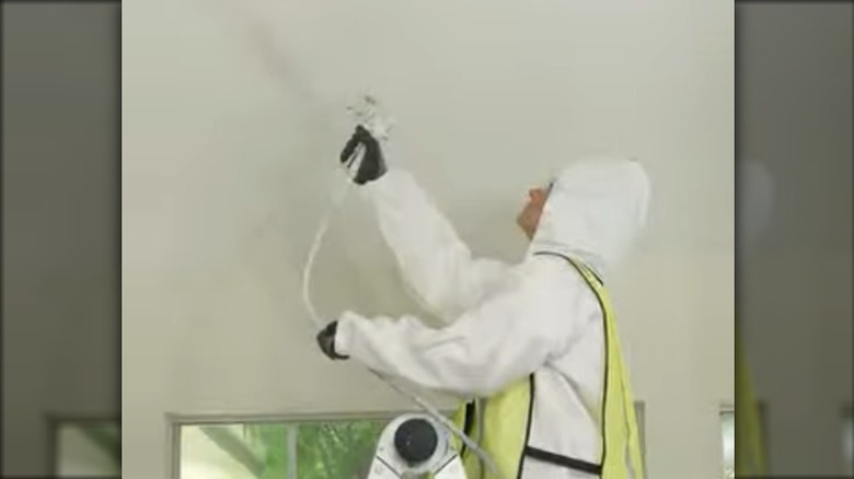 HGTV's Jenn Todryk in coveralls spraying a ceiling