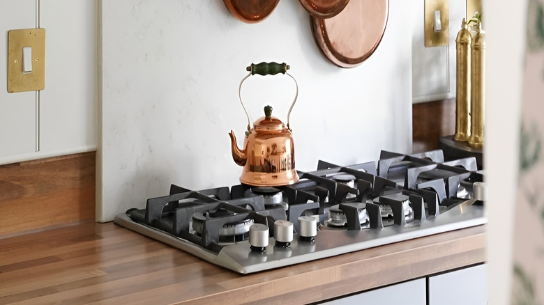 A white kitchen with copper pots hanging from a brass rod above the stove