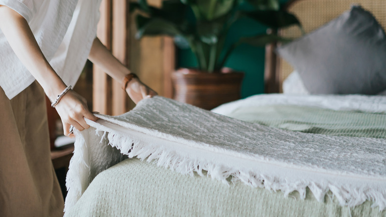 person adding throw blanket to bed