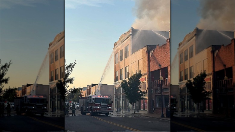 A fire truck blows a jet of water at an old building from which smoke is coming