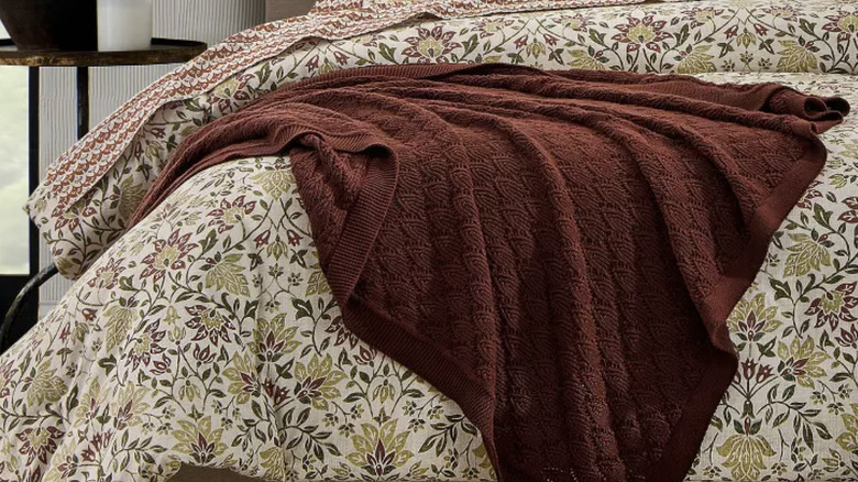 A sheet set in the pattern "Clay Scallop Geo" displayed on a bed along with a "Geneva" comforter set, and  a "Pointelle" throw blanket over the top