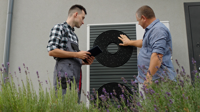 A technician and homeowner stand outside next to a heat pump