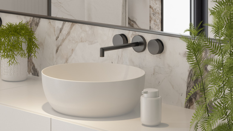 close up of round white modern bathroom sink basin with black matte wall-mounted faucet