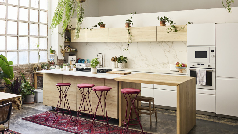 White neutral kitchen with pops of color on red stools, rug, and green indoor plants