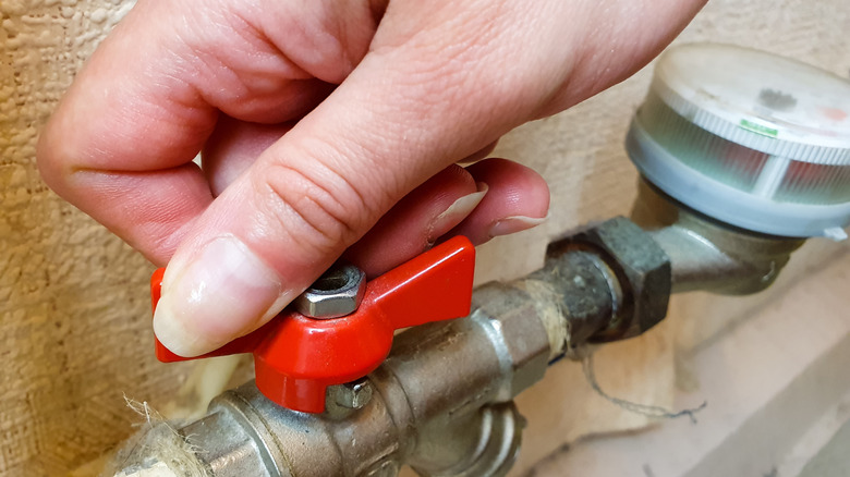 A hand closing a red valve on a metal pipe