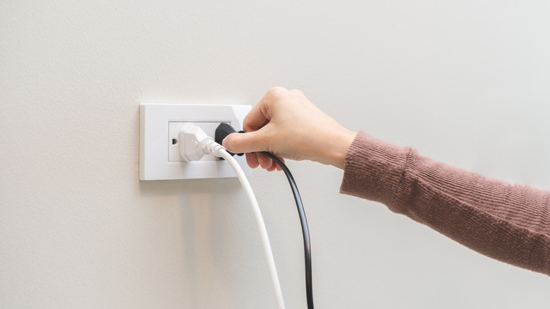 A hand unplugging a stripped cord from an outlet