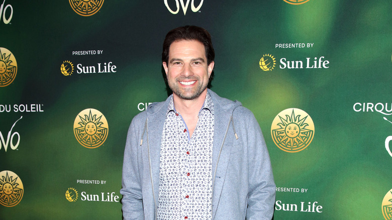 TV host Scott McGillivray at an event with a green logo-filled billboard behind him.
