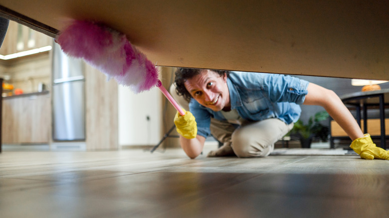 A person cleans under a bed with a pink duster