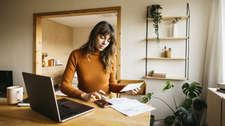 Woman with brown hair wearing an orange turtleneck working at a desk in her home office