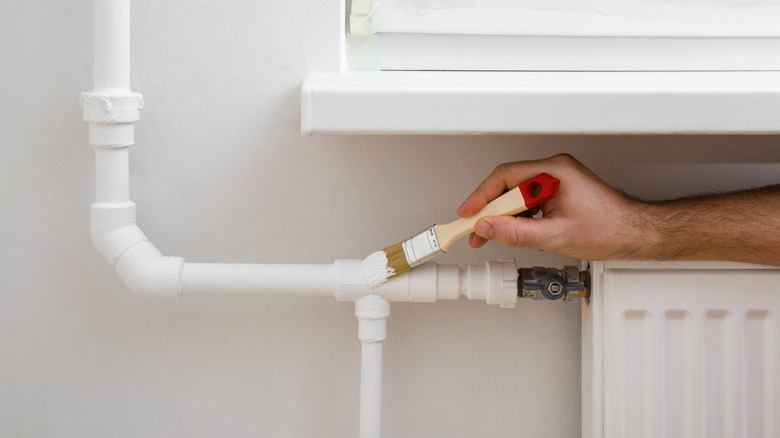 person painting an exposed radiator pipe with white paint
