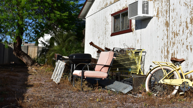 A collection of old furniture and junk piled up in a yard next to a rundown house