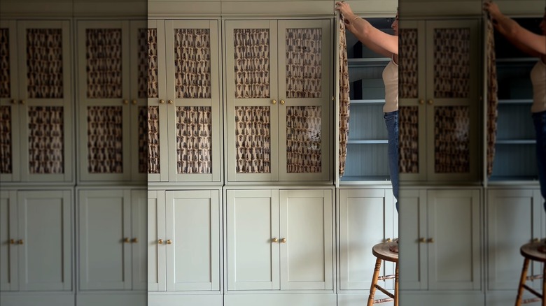 Woman hanging curtains inside glass cabinet door.
